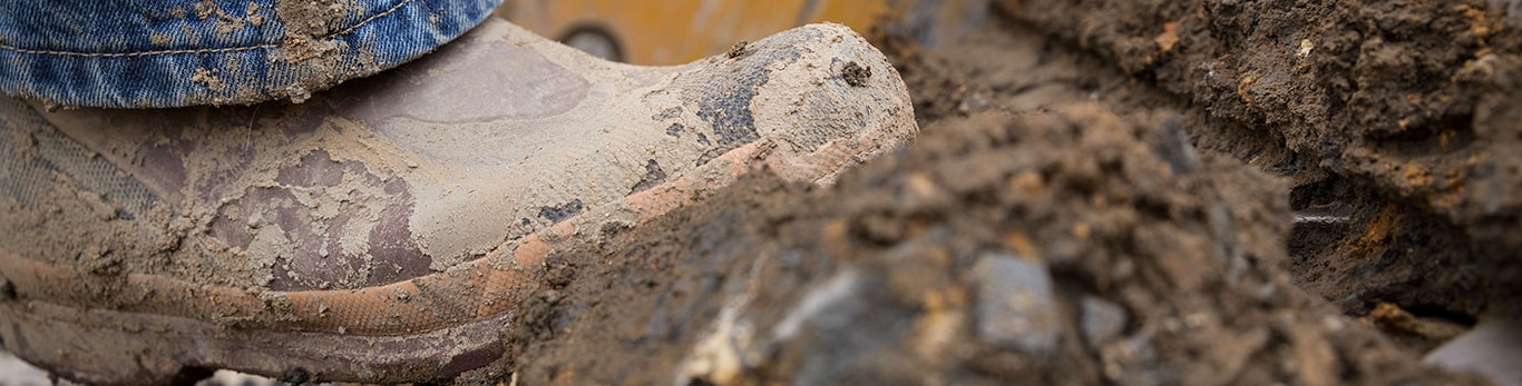 Close-up of a muddy boot stepping up on a muddy machine track