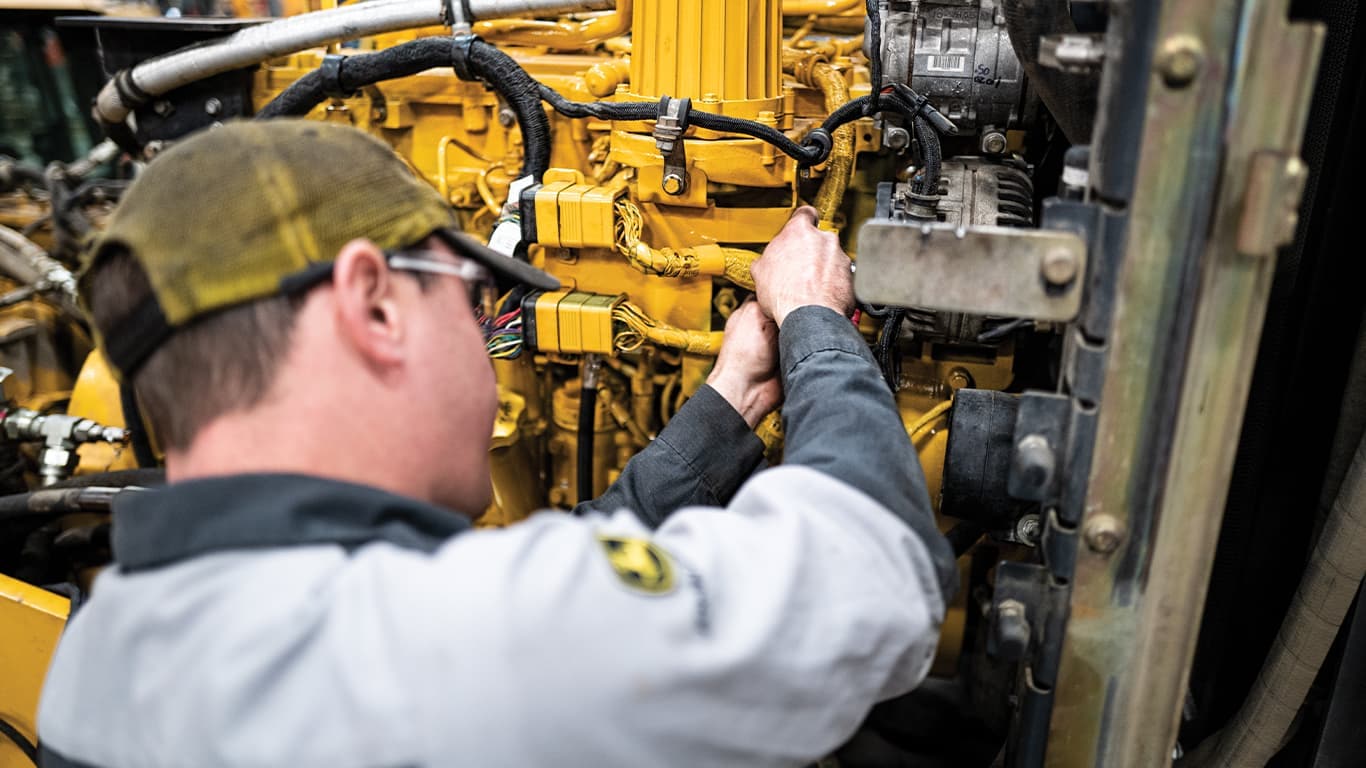A man wearing safety goggles while working on a John Deere engine